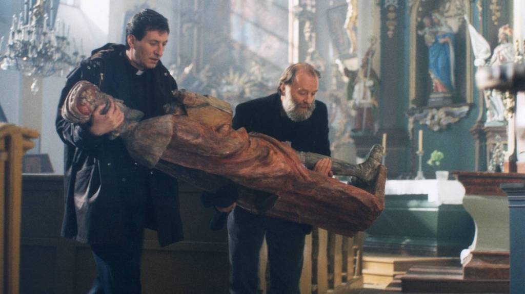 Father Holy and his sculptor friend carrying a religious statue in Forgotten Light